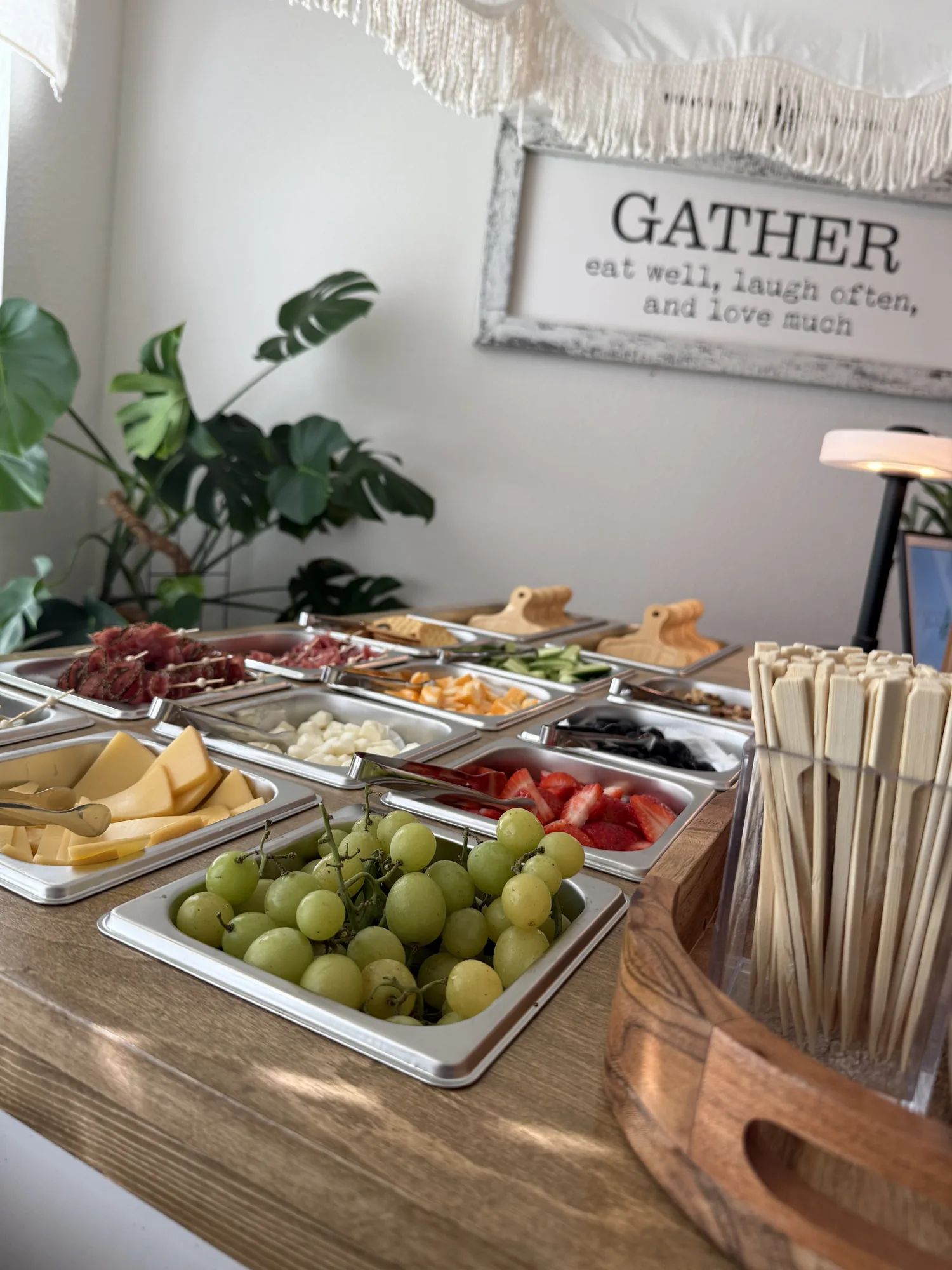 Charcuterie cart stocked with pans of cheese, salami, grapes, strawberries and cucumbers beside bamboo skewers