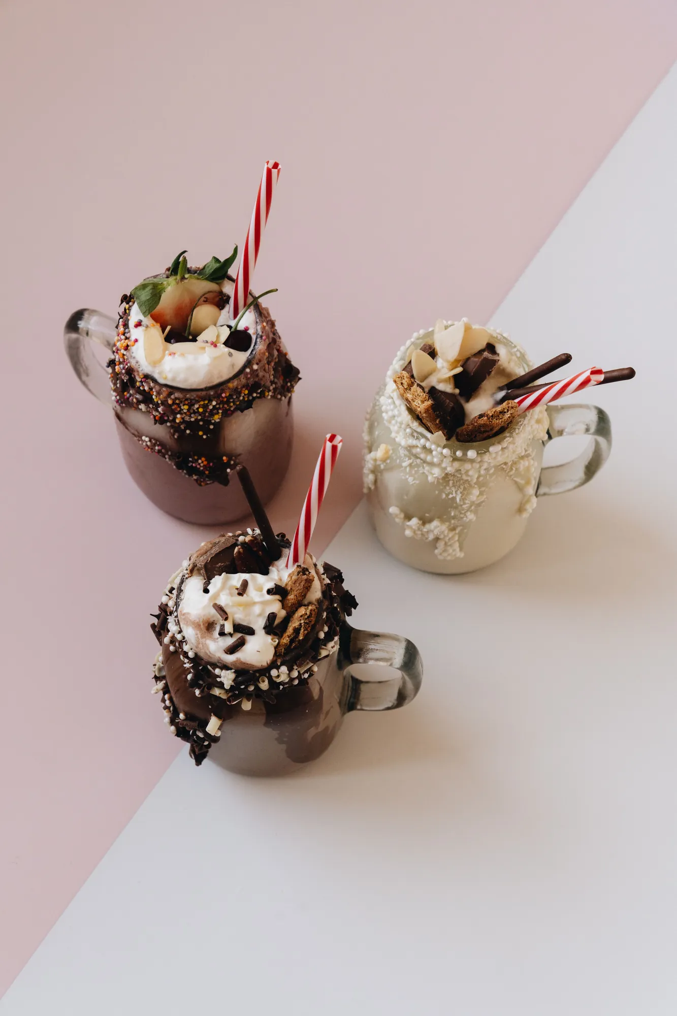 Three hot chocolates topped with whipped cream, chocolate pieces and candy cane straws