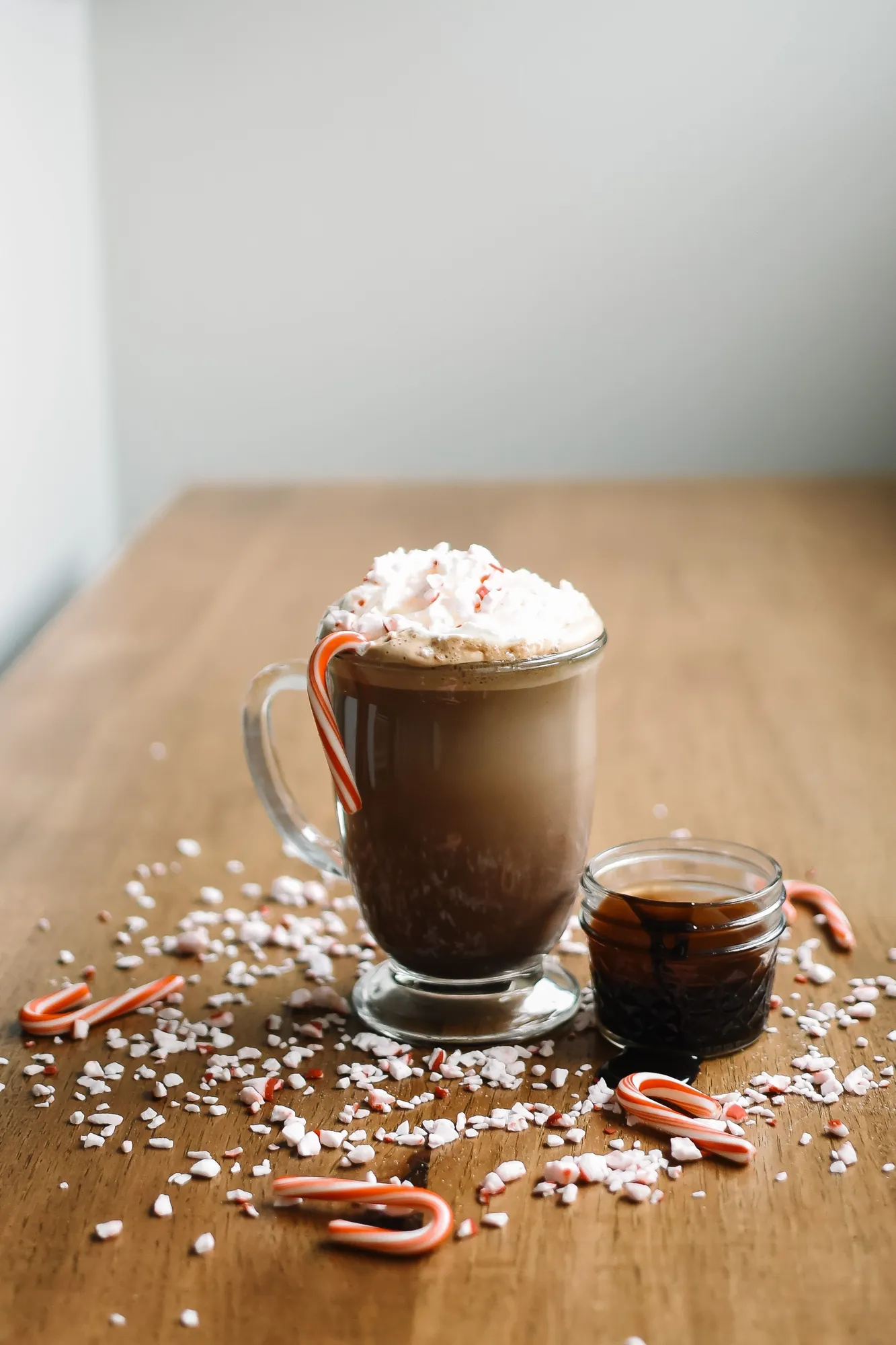 Hot chocolate topped with whipped cream and crushed candy cane, with candy canes scattered on a wood table