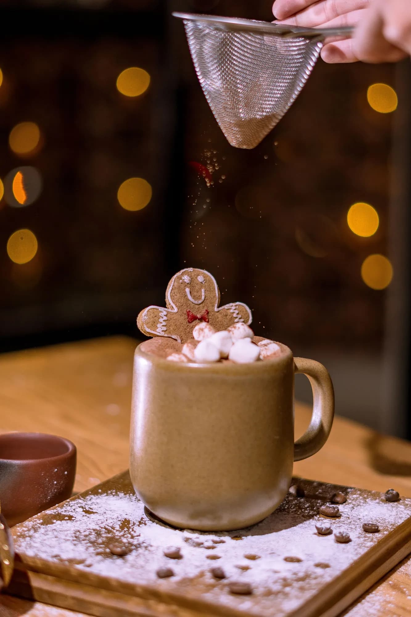 Mug of hot cocoa with marshmallows and a gingerbread cookie being dusted with cocoa