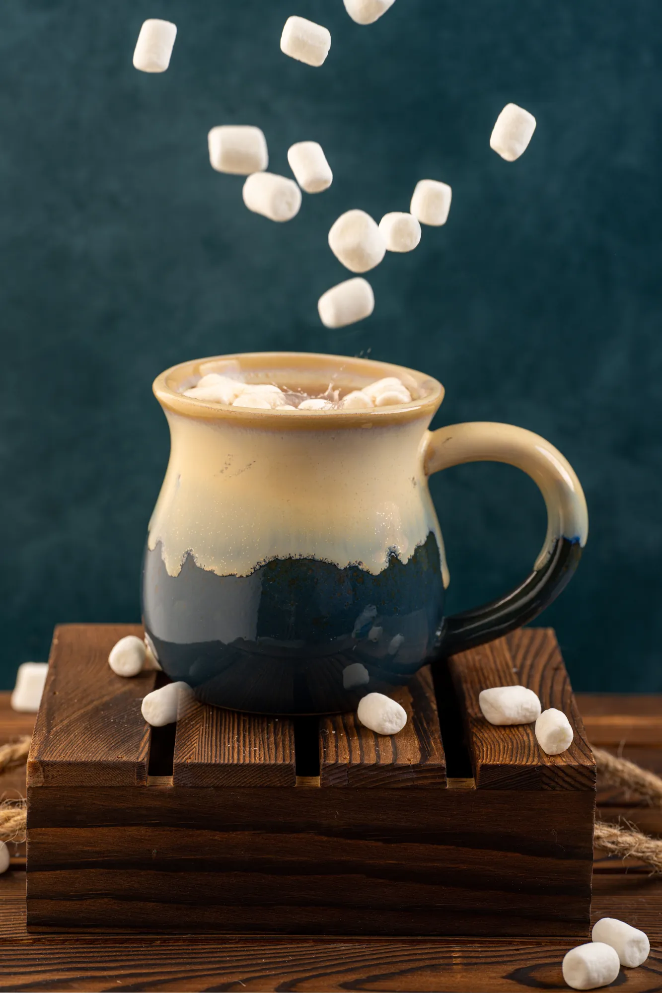 Marshmallows falling into a mug of hot cocoa on a wooden stand