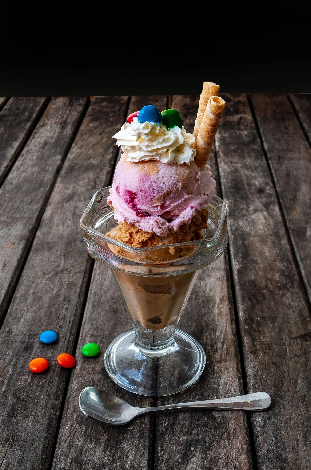 Ice cream sundae with whipped cream, M&M's and a wafer roll in a glass on a wood table