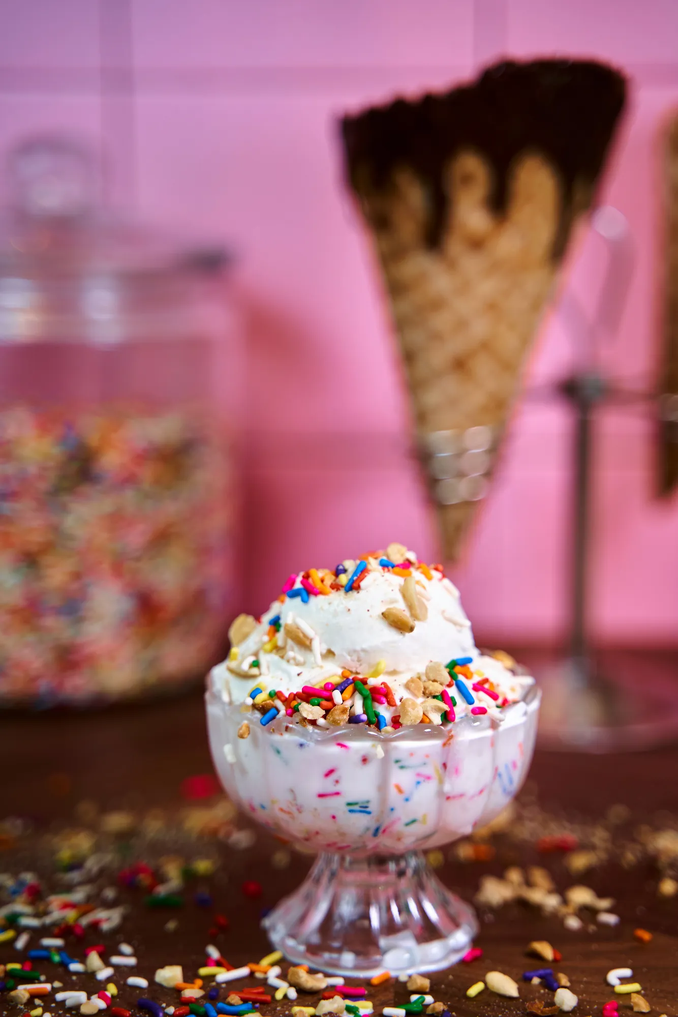 Ice cream sundae covered in rainbow sprinkles and nuts in a glass dish