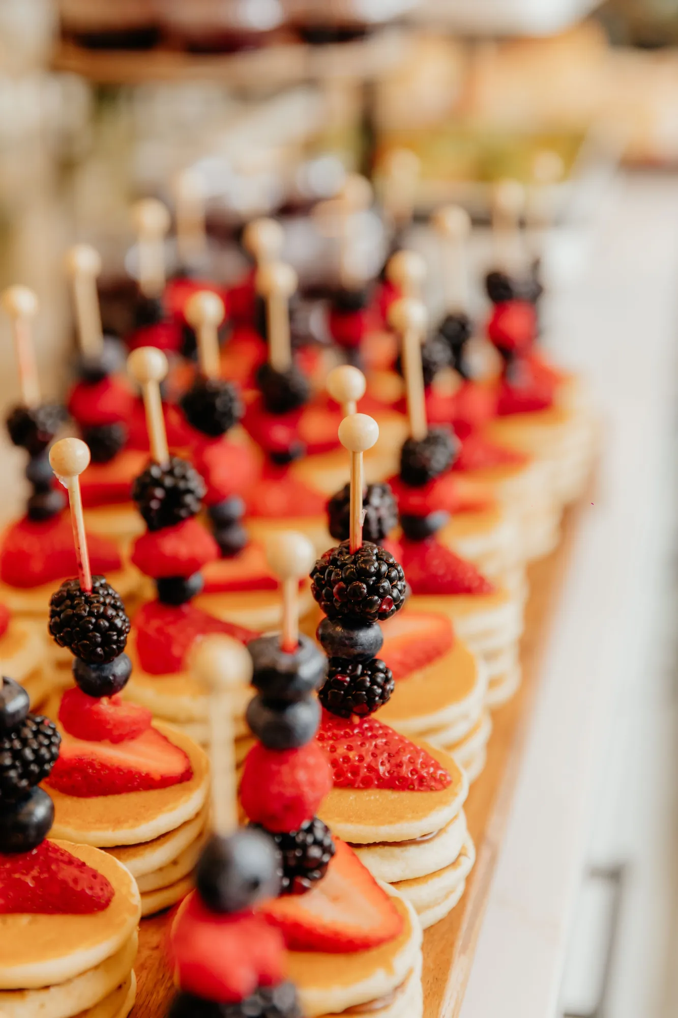 Rows of mini pancake stacks topped with strawberries, blueberries and blackberries on skewers