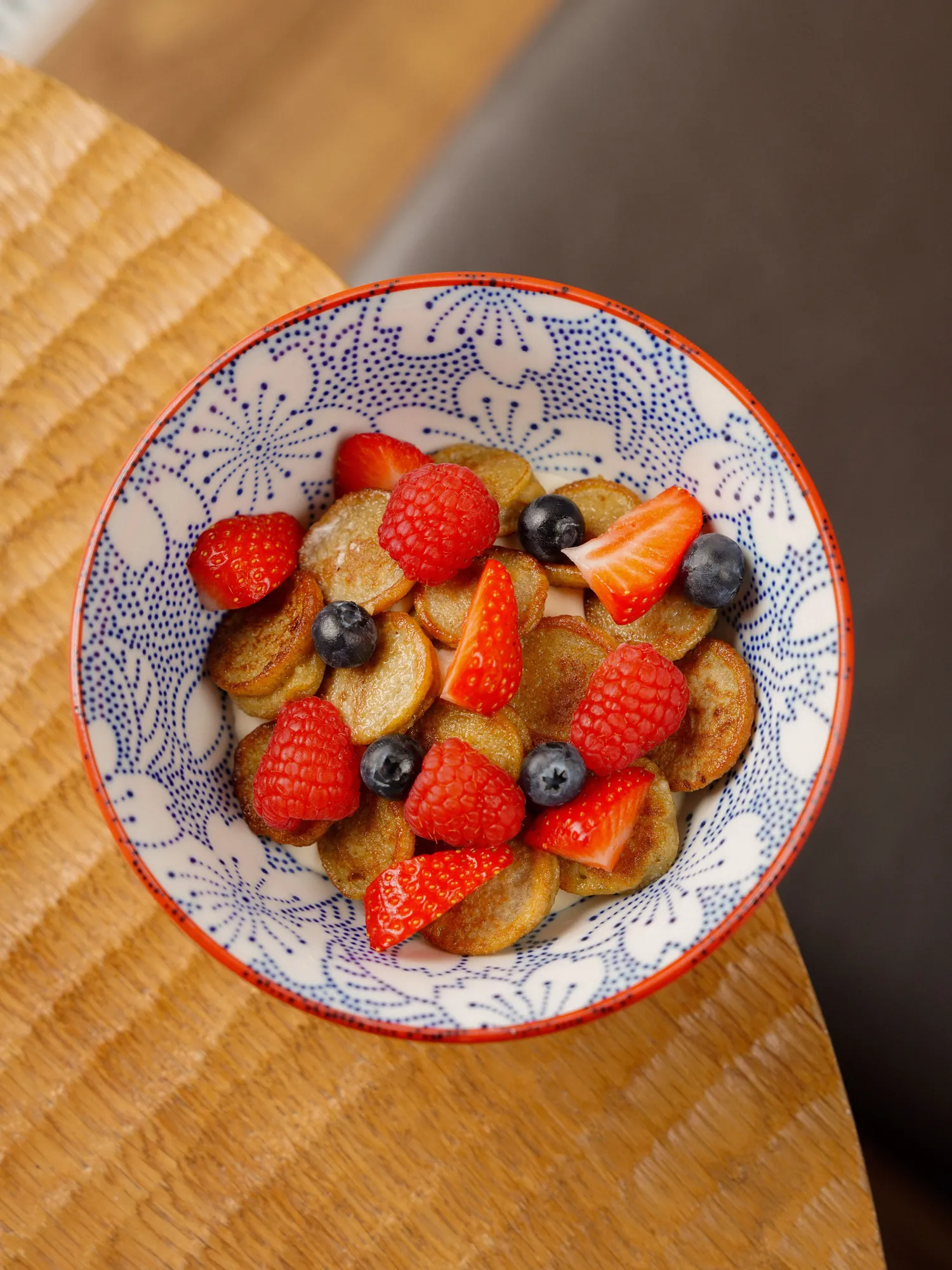 Bowl of mini pancakes topped with fresh strawberries and blueberries