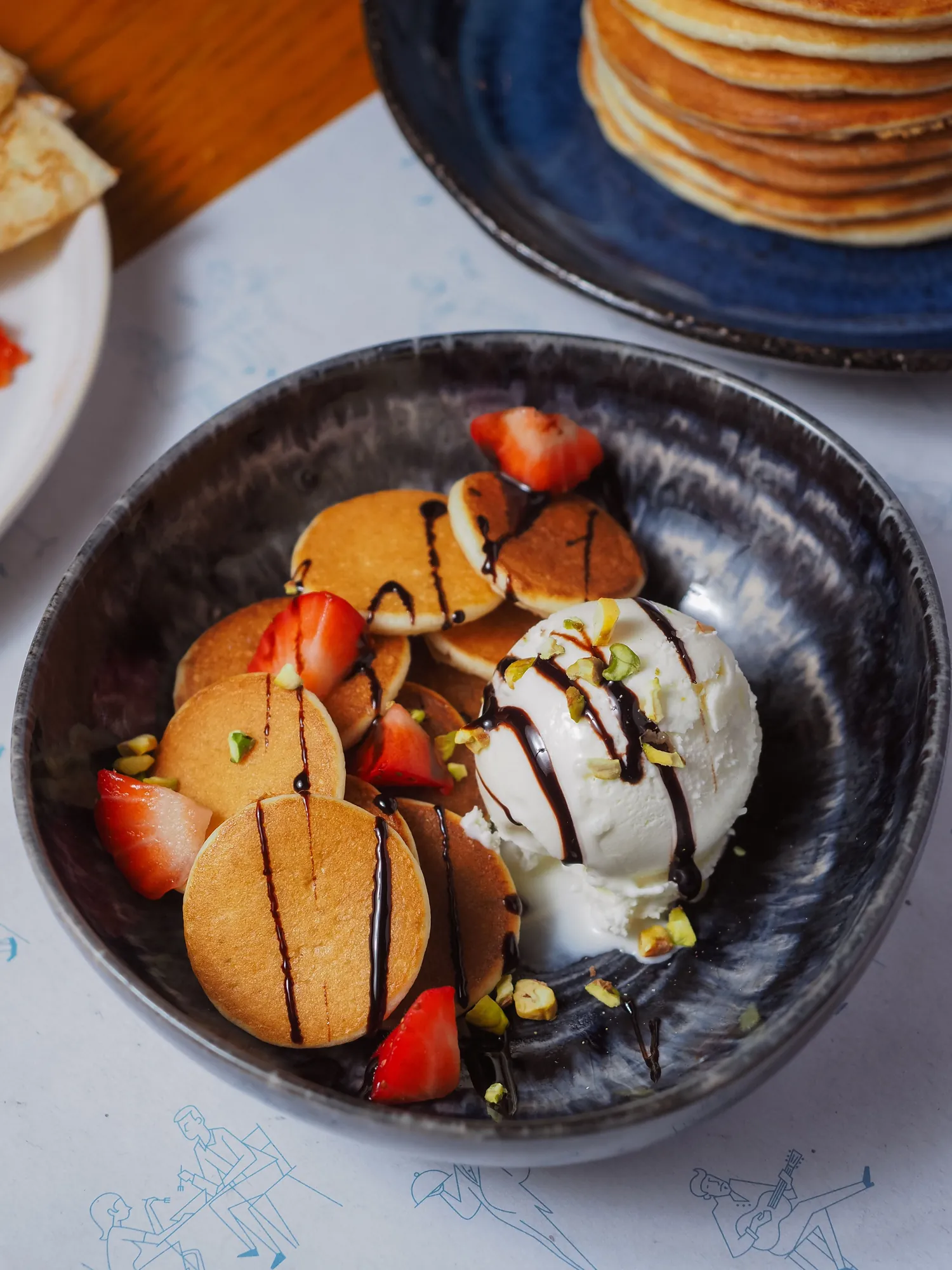 Mini pancakes with strawberries, chocolate drizzle, pistachios and a scoop of ice cream